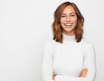 Woman in white sweater with arms crossed smiling in front of white background